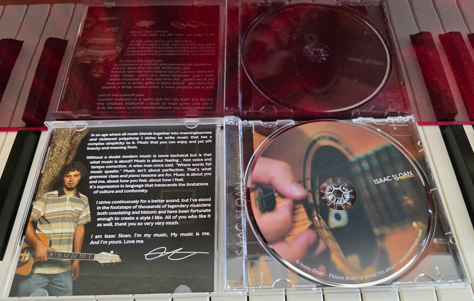 CD jewel cases for Isaac Sloan's As Promised album arranged on piano keys.